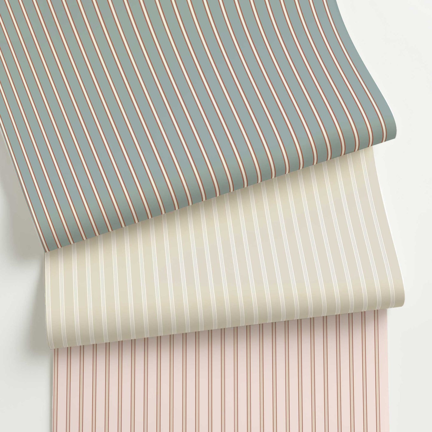 Three rolls of Lachman custom wide ticking stripe wallpaper in muted blue, ivory, and blush colorways, featuring spaced-out traditional stripe patterns.