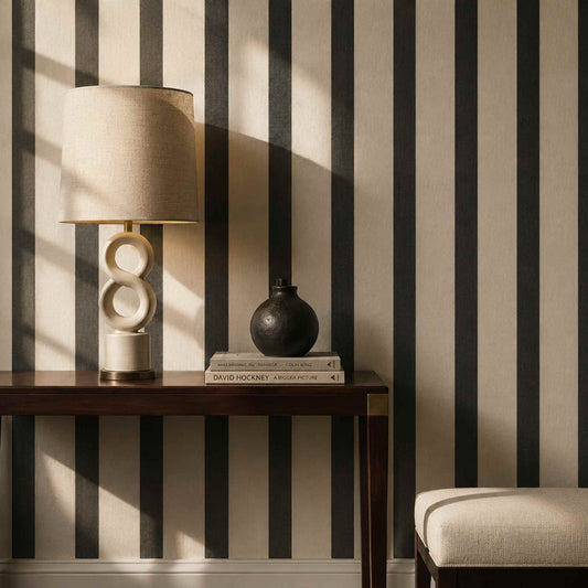 A modern, decorative lamp on a side table, against a black and cream striped wall with art books and a vase.