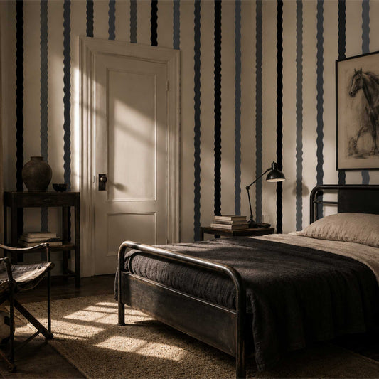 Bedroom with surreal, wavy striped wallpaper in white, grey and black, with vintage bed, lamp, and door.