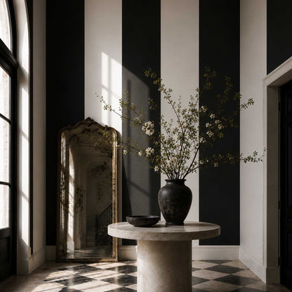 Grand entryway with extra wide black and white striped wallpaper, checkered floors, a stone table with a vase of cherry branches, and decorative mirror.