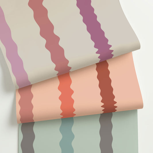 Three colorways of Maiden, a playful wavy stripe wallpaper with hand-drawn curves in warm, modern palettes—rolled to show variety and texture.