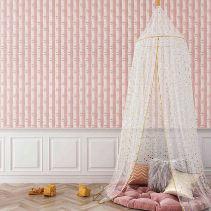 Children's room with a canopy over a pink cushion on the floor against a pink wallpapered wall. Rose Pink striped Shibori Bamboo Wallpaper styled in a light-filled interior space
